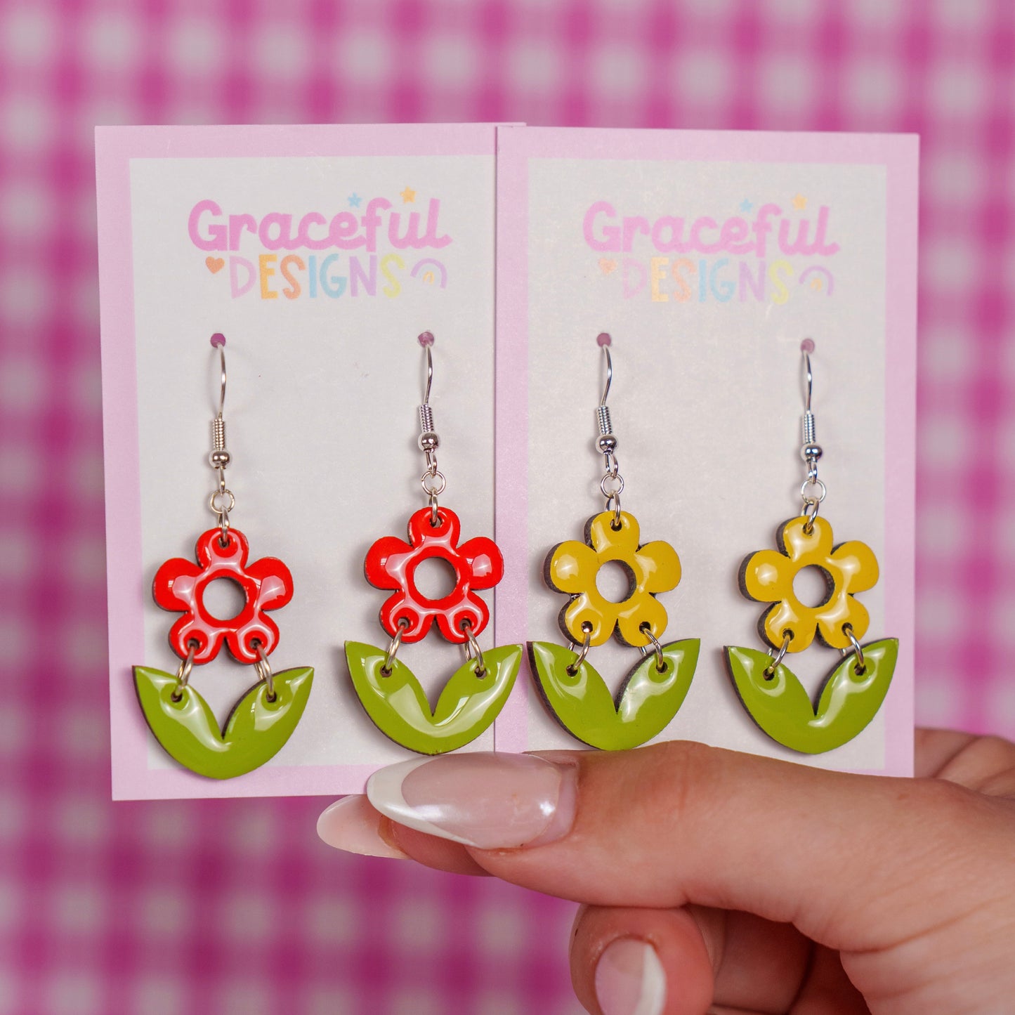 Colorful flower-shaped earrings on a 'Graceful Designs' card held against a pink checkered background.