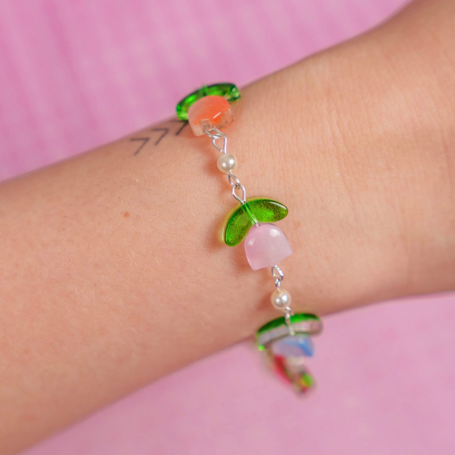 Bracelet with colorful beads on a wrist against a pink background