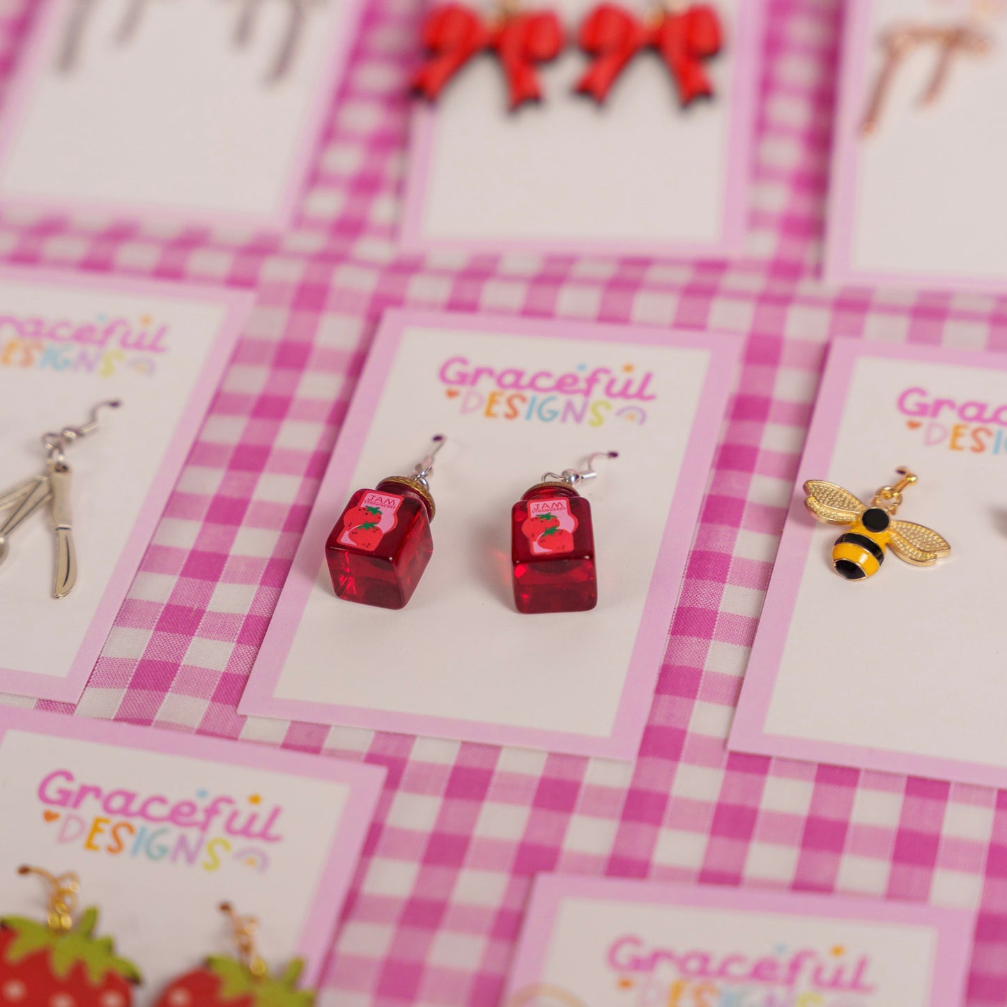 Earrings on cards with 'Graceful Designs' branding on a pink checkered background