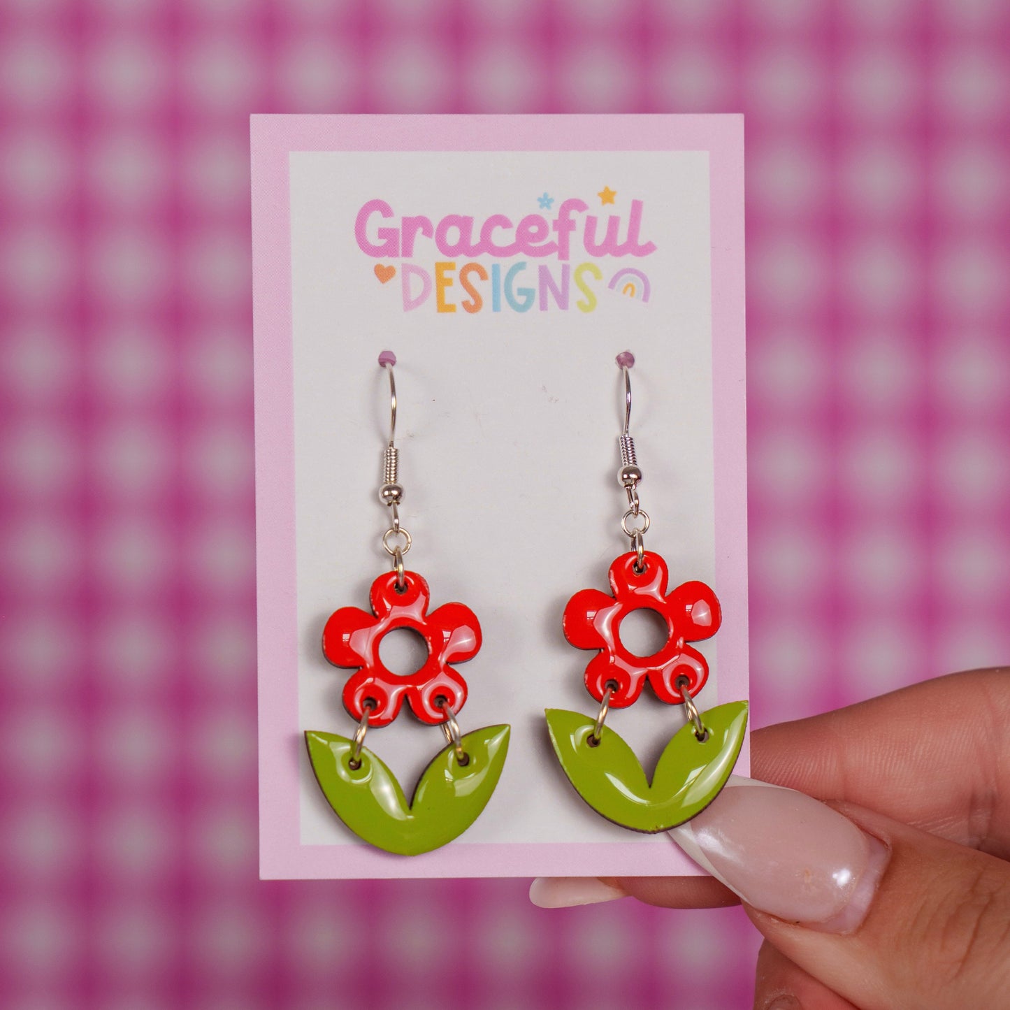 Flower-shaped earrings on a 'Graceful Designs' card against a pink checkered background