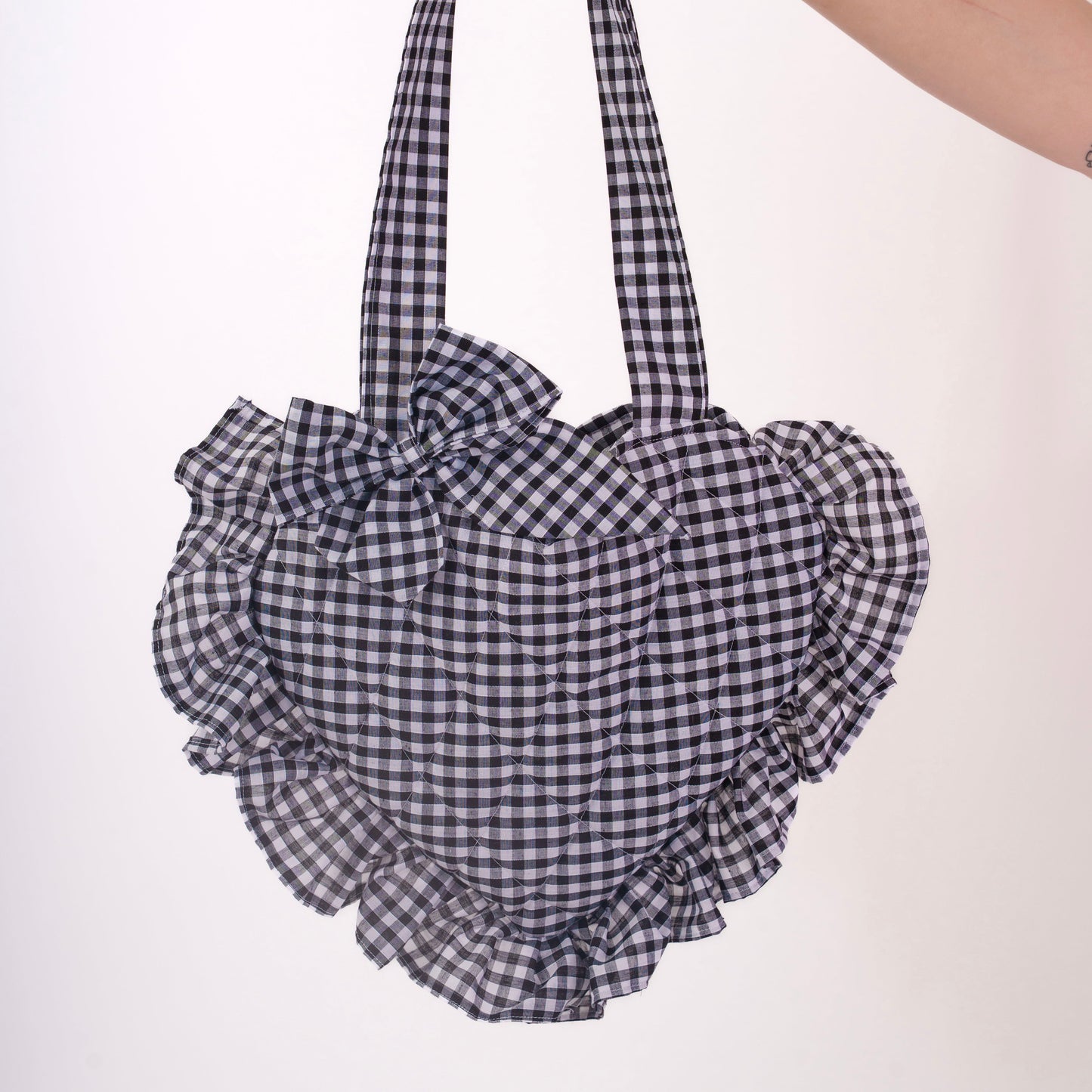 Hand holding a black and white checkered bag with ruffled details on a white background