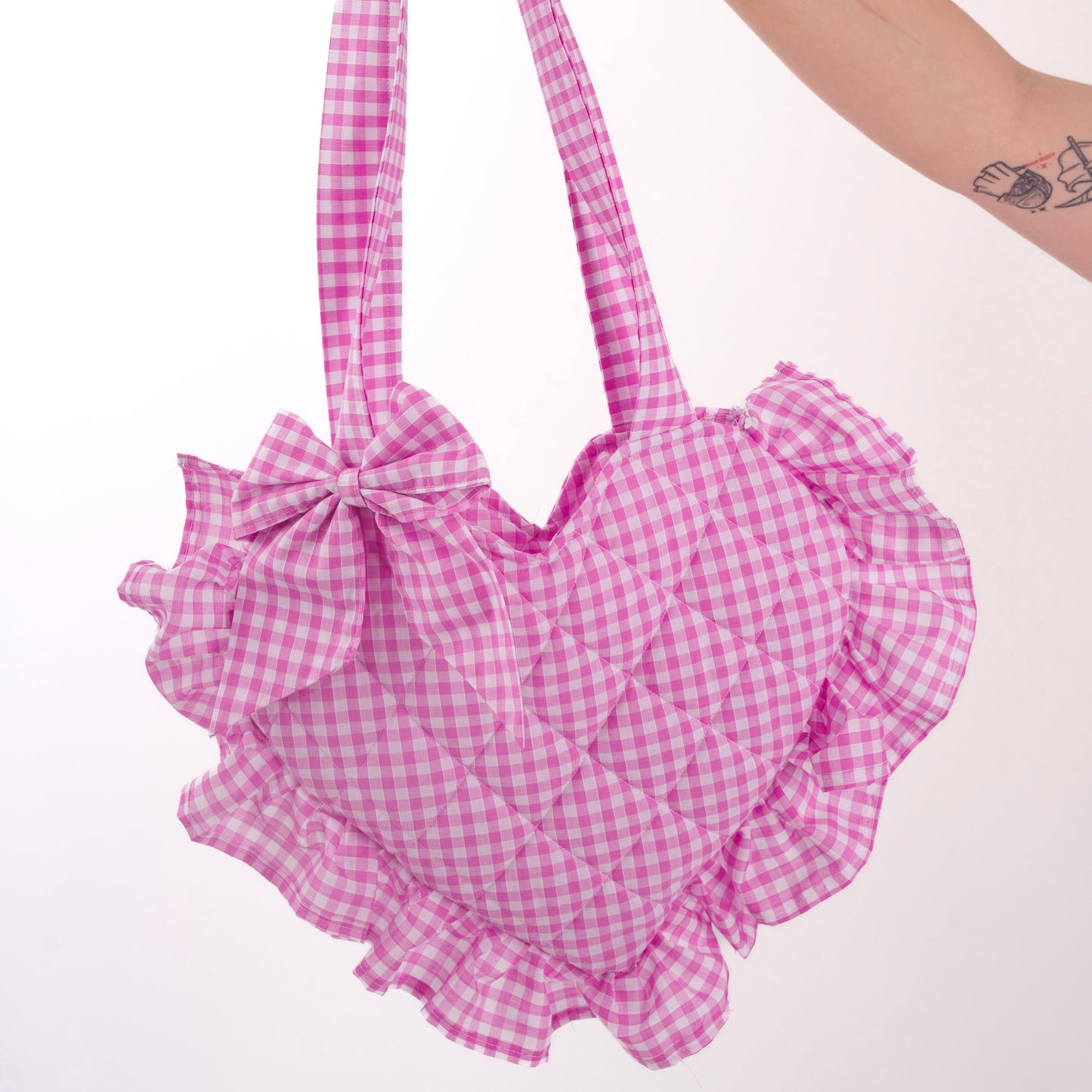 Pink gingham handbag with ruffles held by a hand on a white background