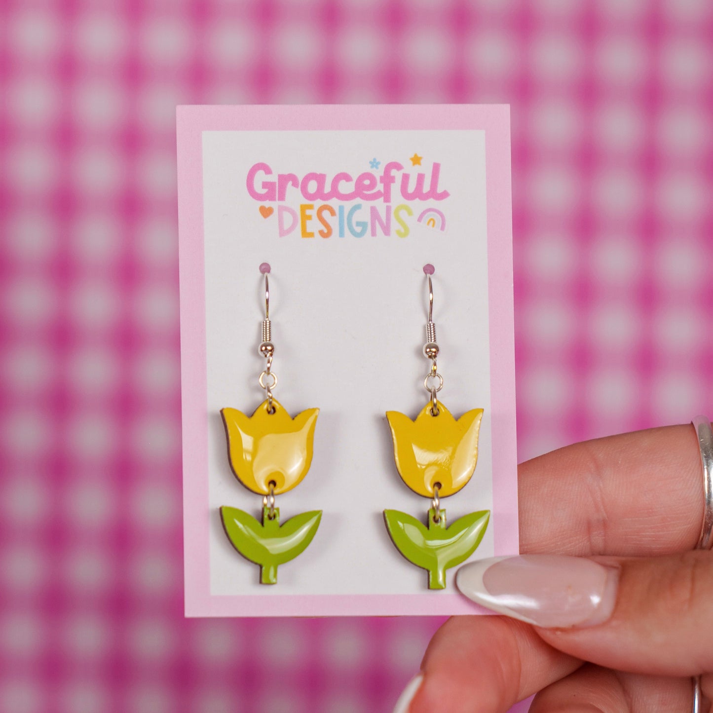 Yellow and green tulip-shaped earrings on a 'Graceful Designs' card against a pink checkered background.