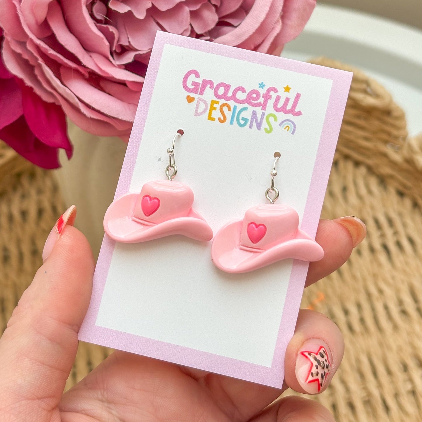 Pink bow-shaped earrings on a 'Graceful Designs' card with a pink flower in the background