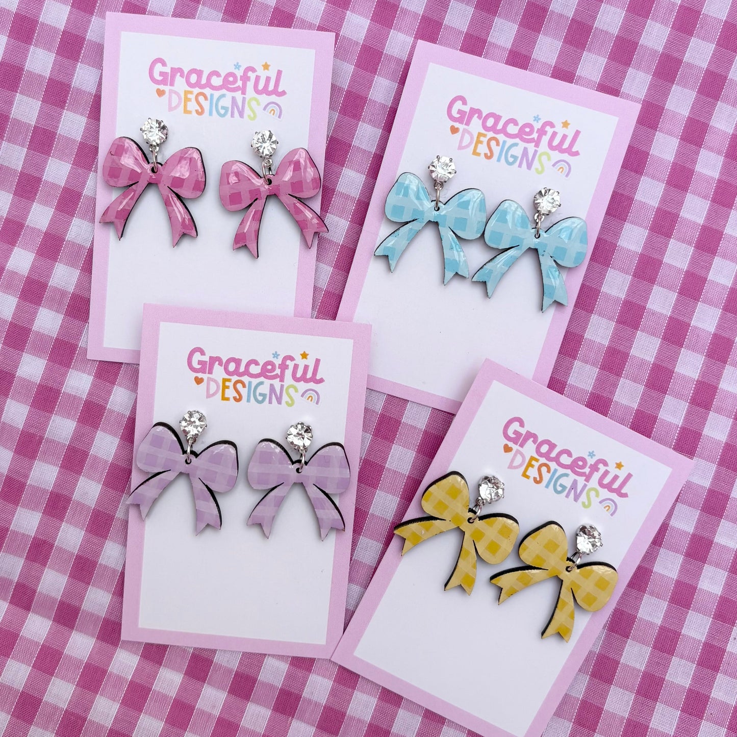 Set of bow-shaped earrings on cards with 'Graceful Designs' branding on a pink checkered background.