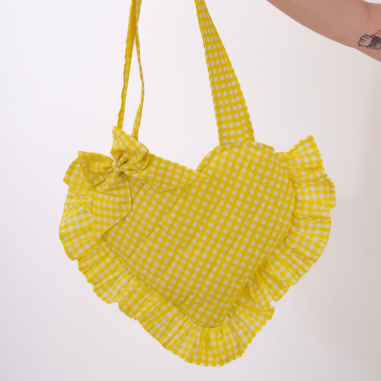 Yellow gingham handbag with ruffled edges held by a hand on a white background