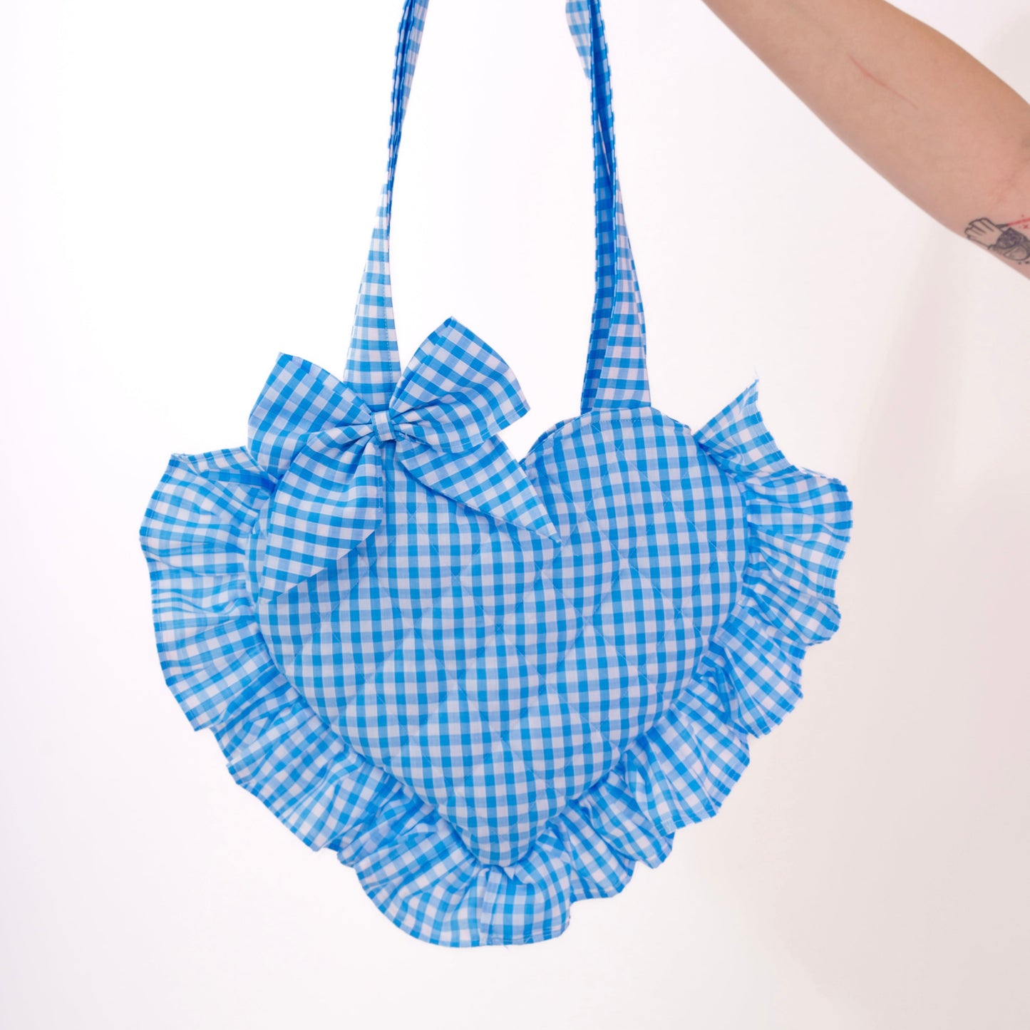 Blue gingham handbag with ruffles held by a hand on a white background