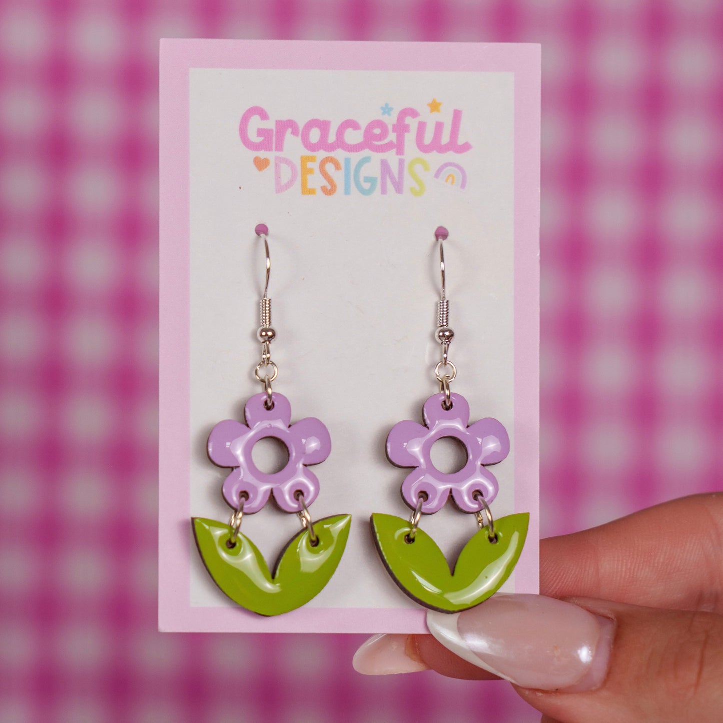 Flower-shaped earrings on a 'Graceful Designs' card against a pink and white checkered background