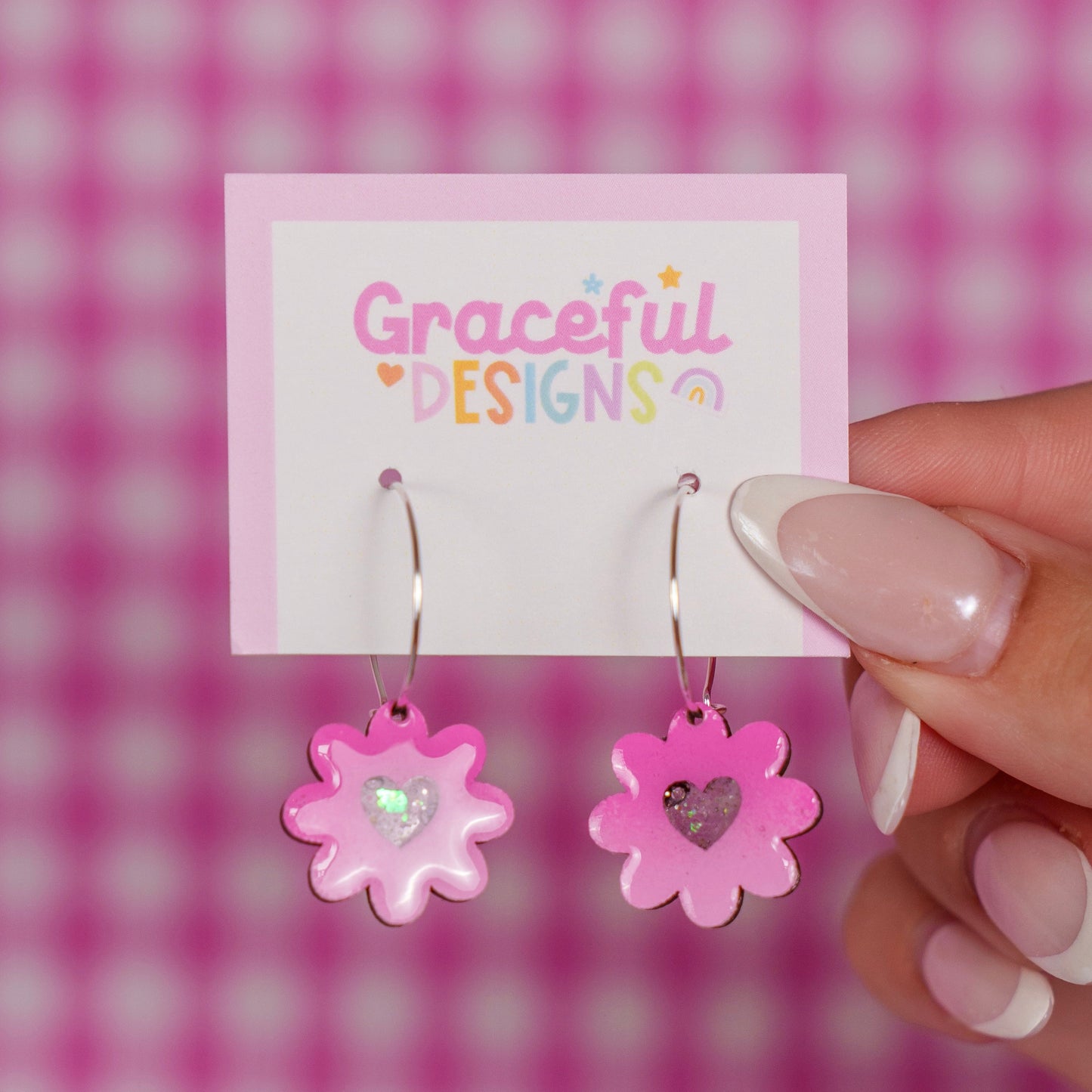 Pink flower-shaped earrings on a 'Graceful Designs' card against a pink checkered background.