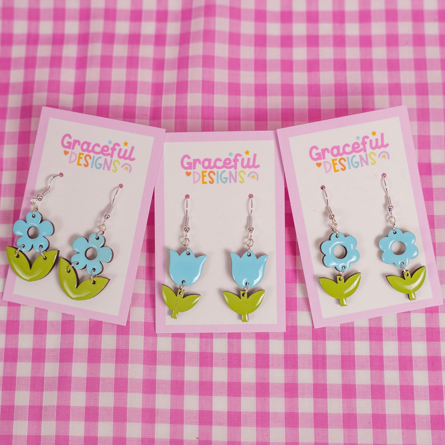 Floral earrings on cards with 'Graceful Designs' branding against a pink checkered background