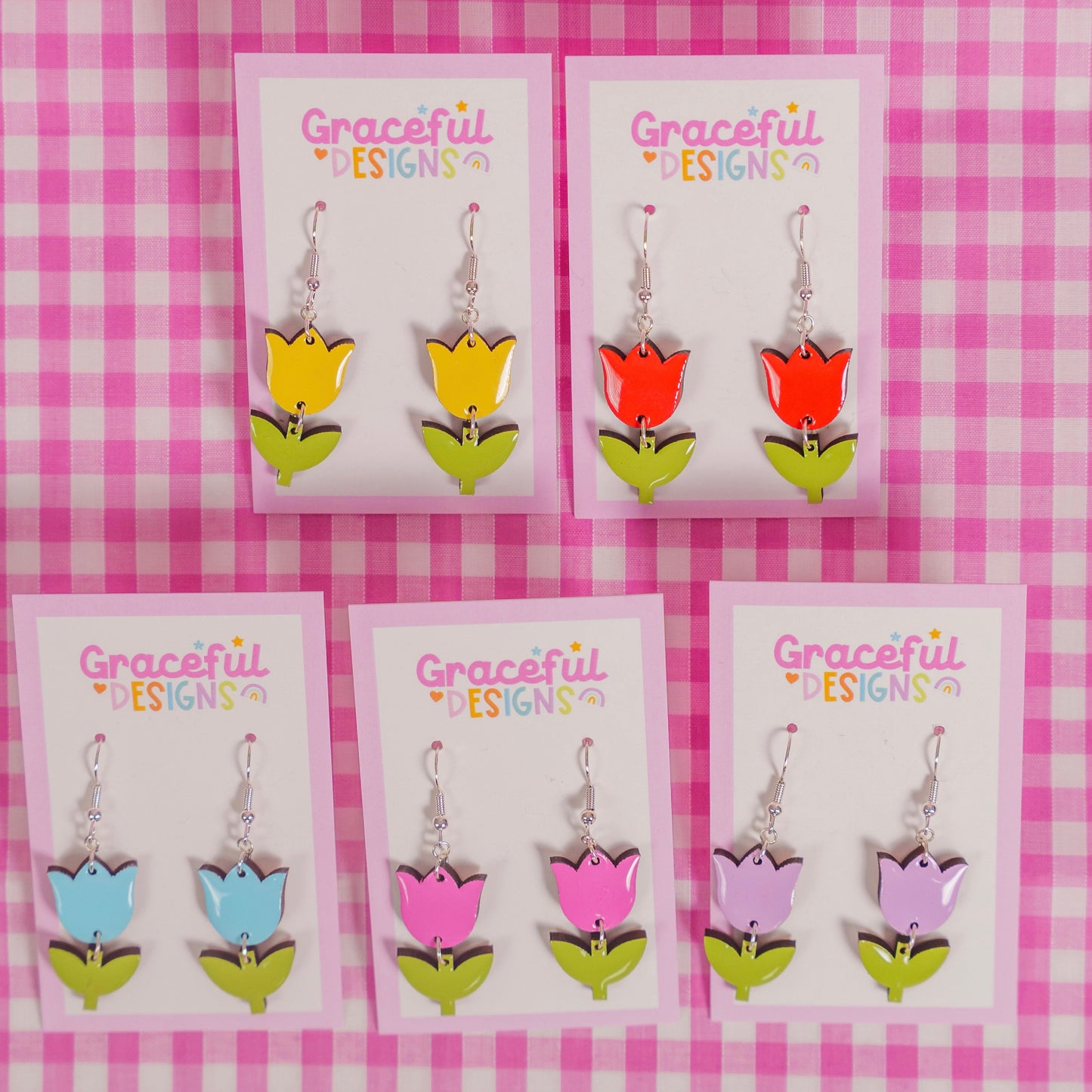 Set of colorful tulip-shaped earrings on 'Graceful Designs' cards against a pink checkered background.