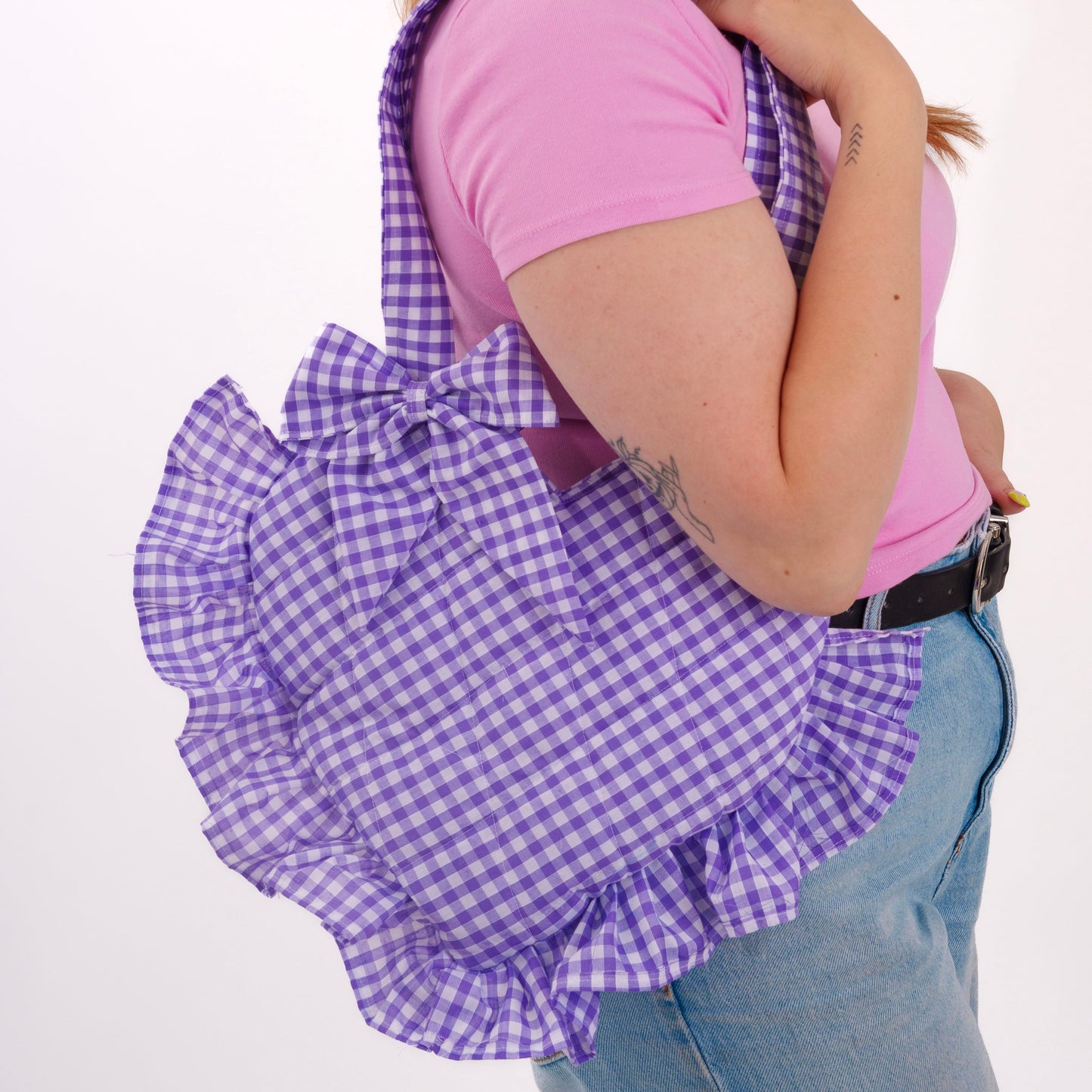 Person wearing a purple gingham apron over a pink shirt on a white background