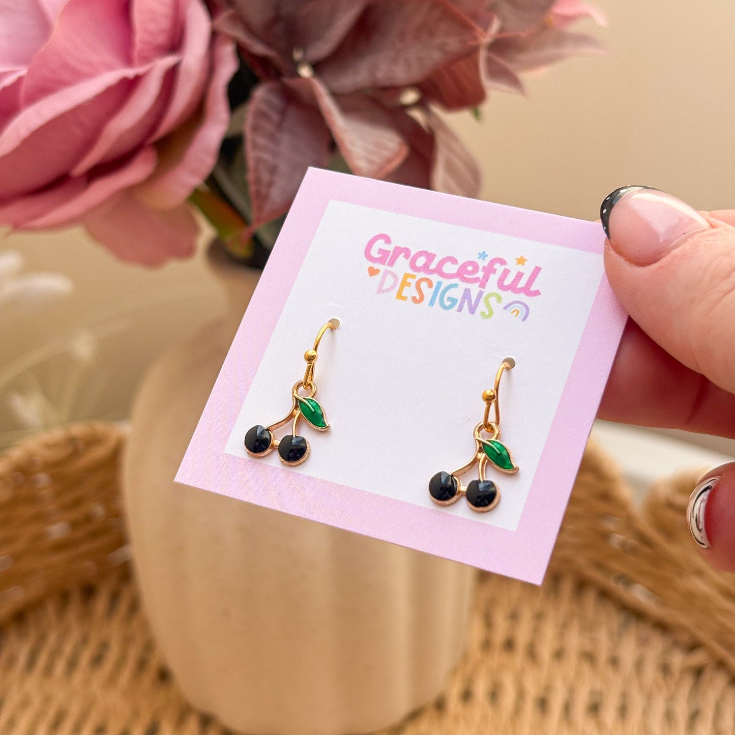 Cherry-themed earrings on a 'Graceful Designs' card with flowers in the background