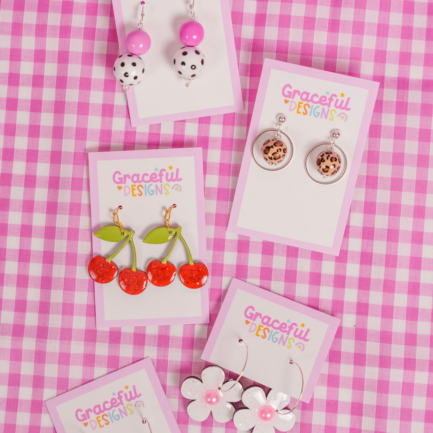 Collection of earrings on cards with 'Graceful Designs' branding on a pink checkered background.