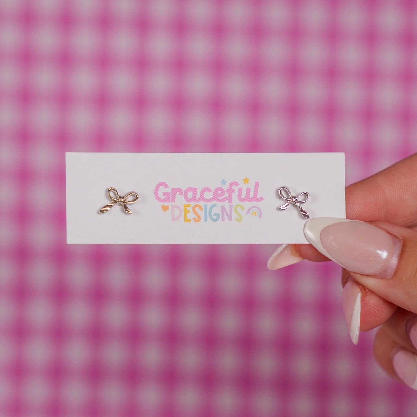 Earrings on a card with 'Graceful Designs' text against a pink checkered background