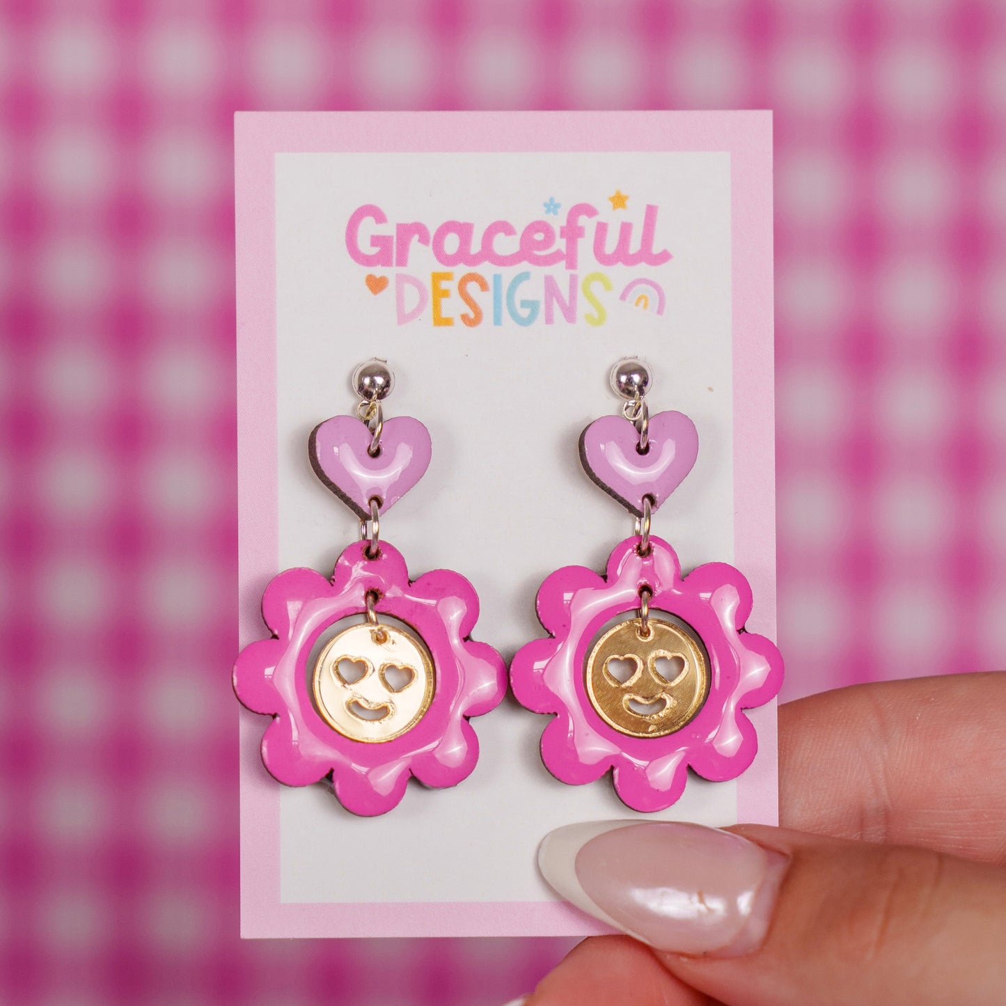 Pink flower-shaped earrings on a 'Graceful Designs' card against a pink checkered background.