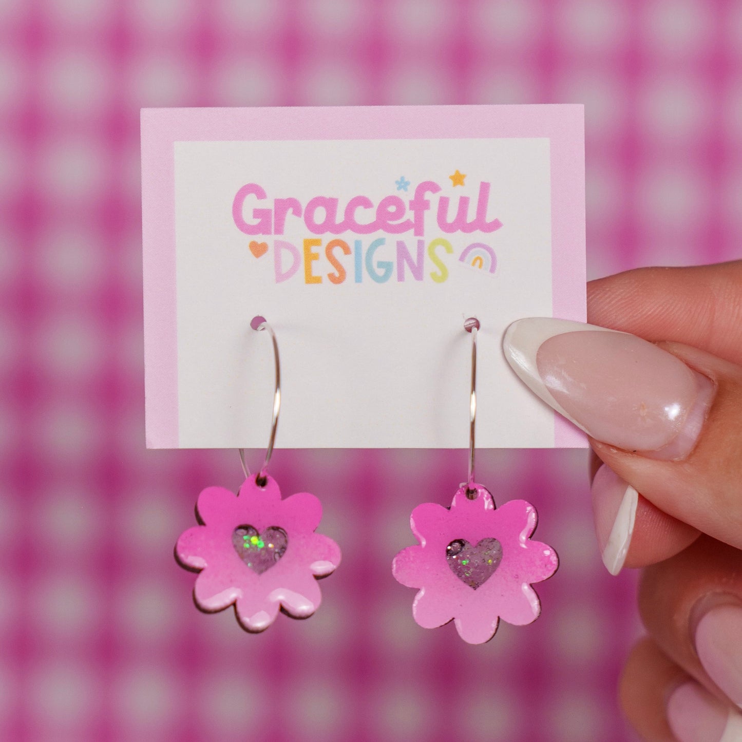 Pink flower-shaped earrings on a 'Gracéful Designs' card against a pink checkered background.