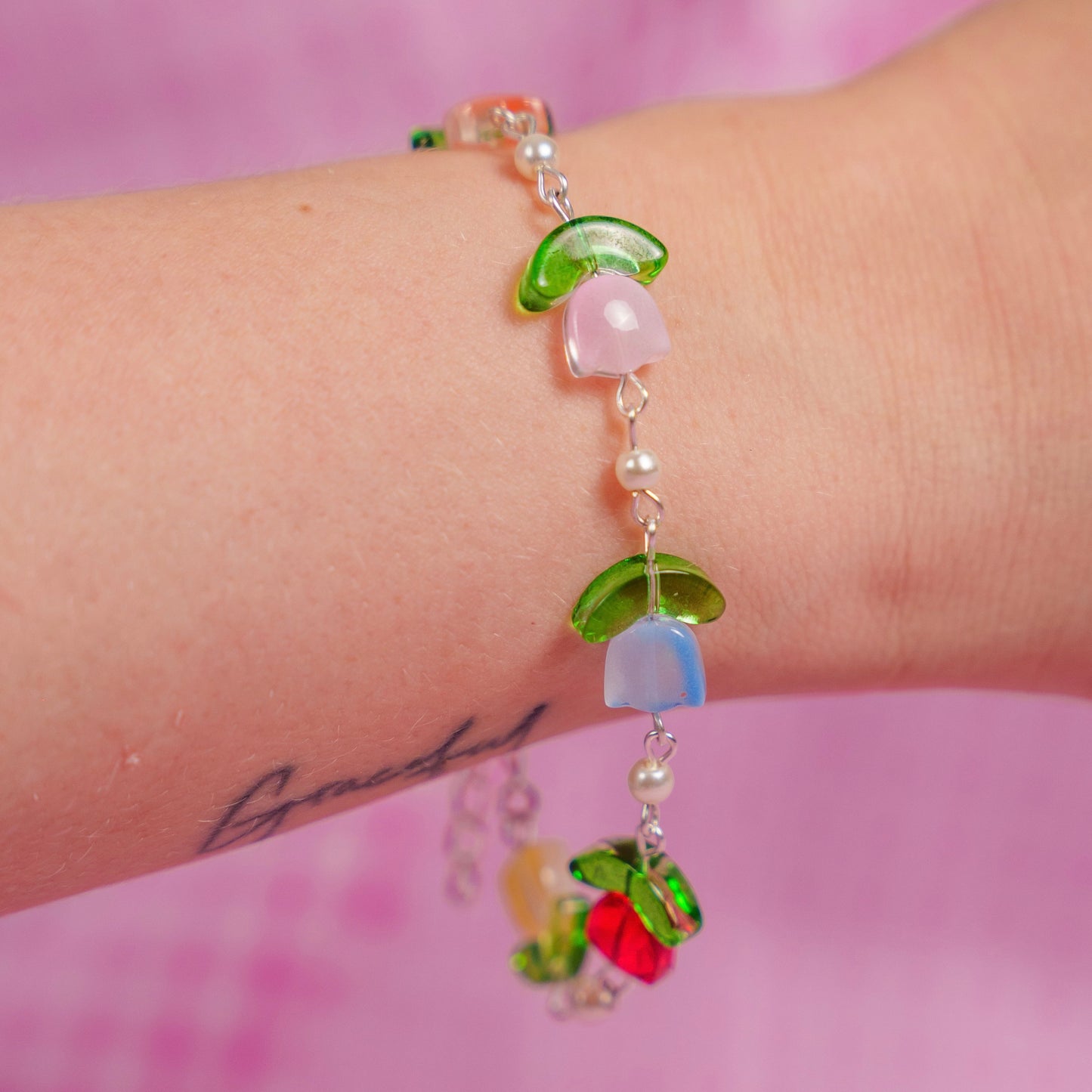 Colorful beaded bracelet on a wrist with a pink background