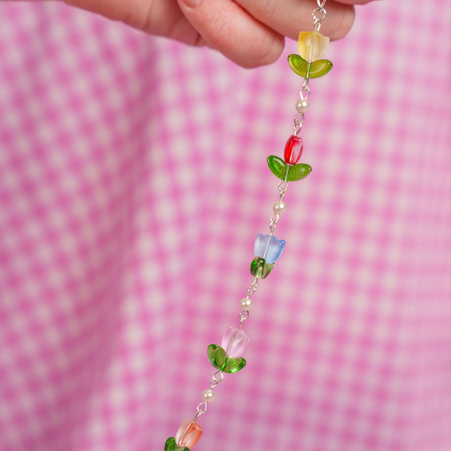 Colorful beaded chain held against a pink checkered background