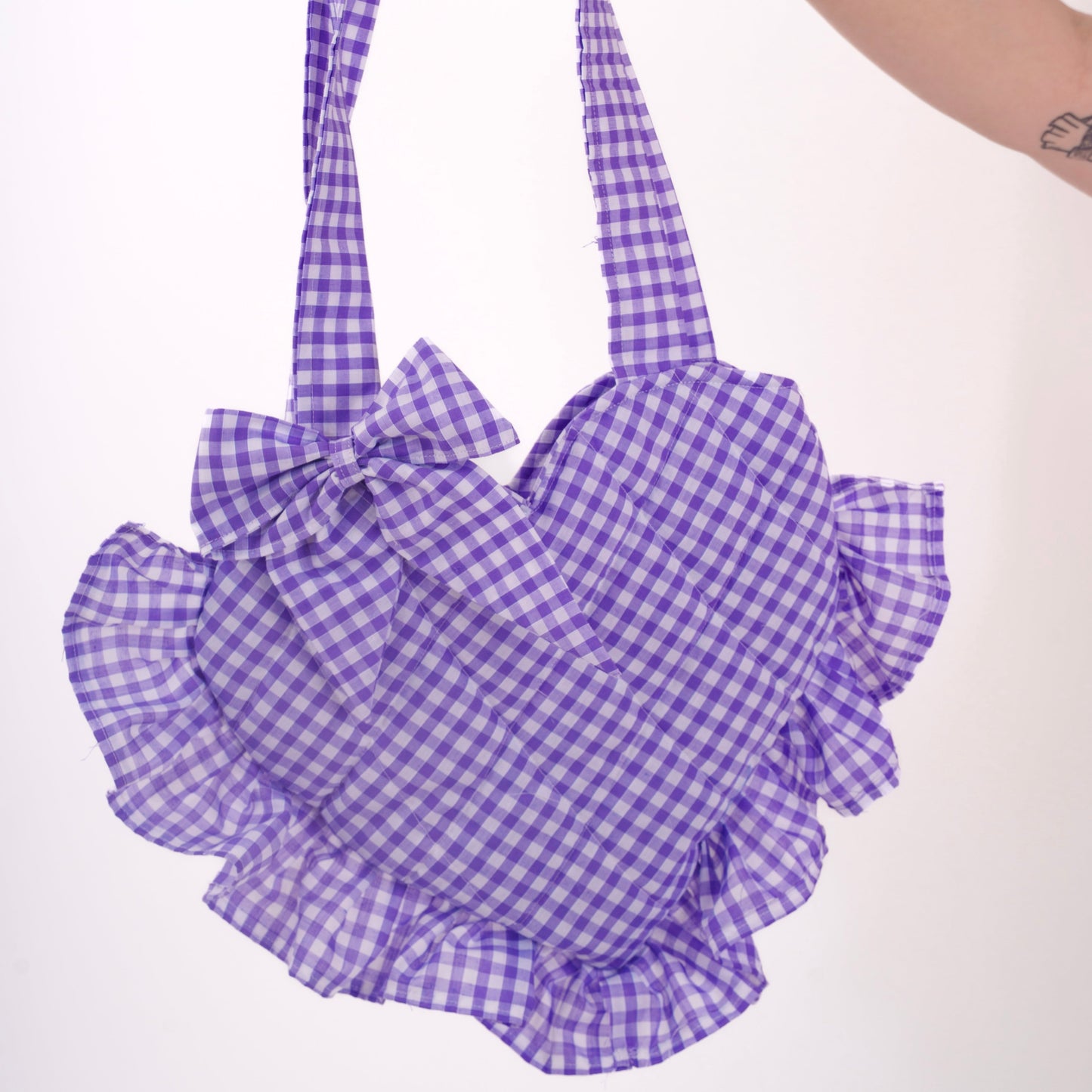 Purple gingham bag with ruffles held by a hand on a white background
