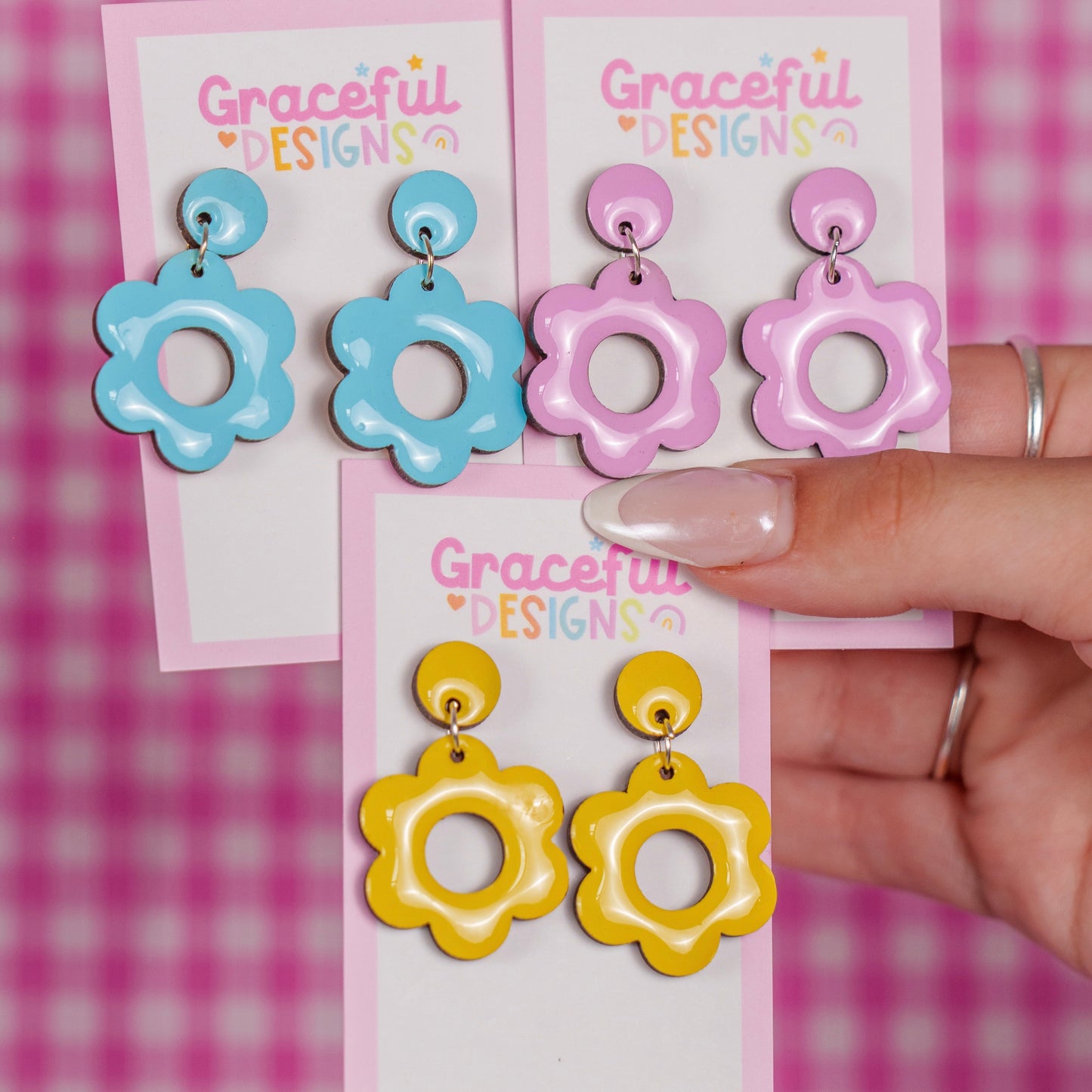 Colorful earrings on 'Graceful Designs' cards held against a pink and white checkered background.