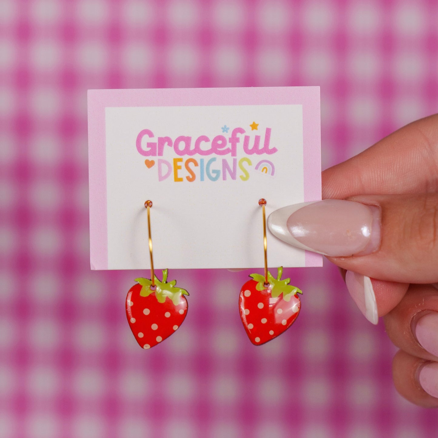 Strawberry-shaped earrings on a 'Graceful Designs' card against a pink checkered background