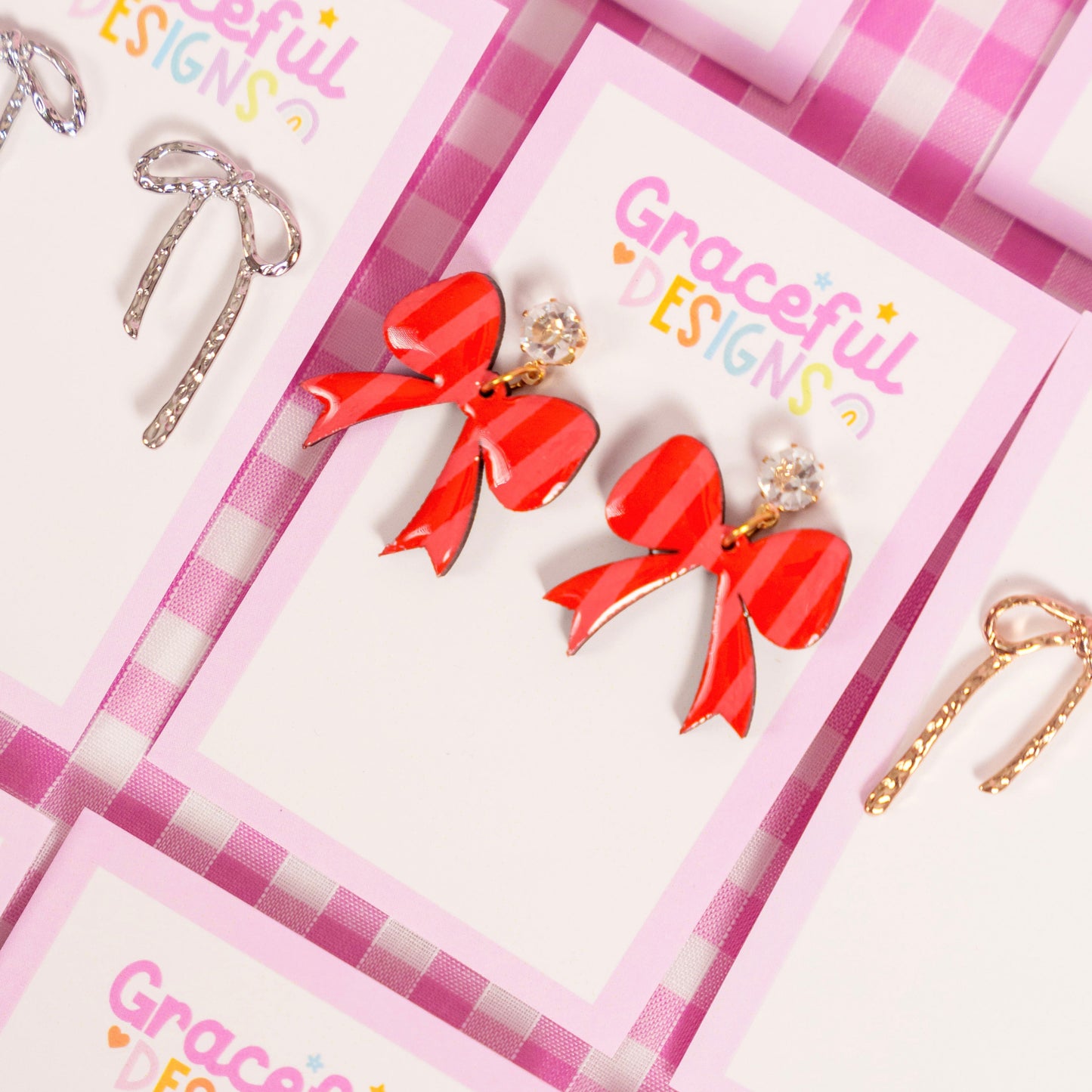 Earrings on display with 'Graceful Designs' branding on pink checkered cards.