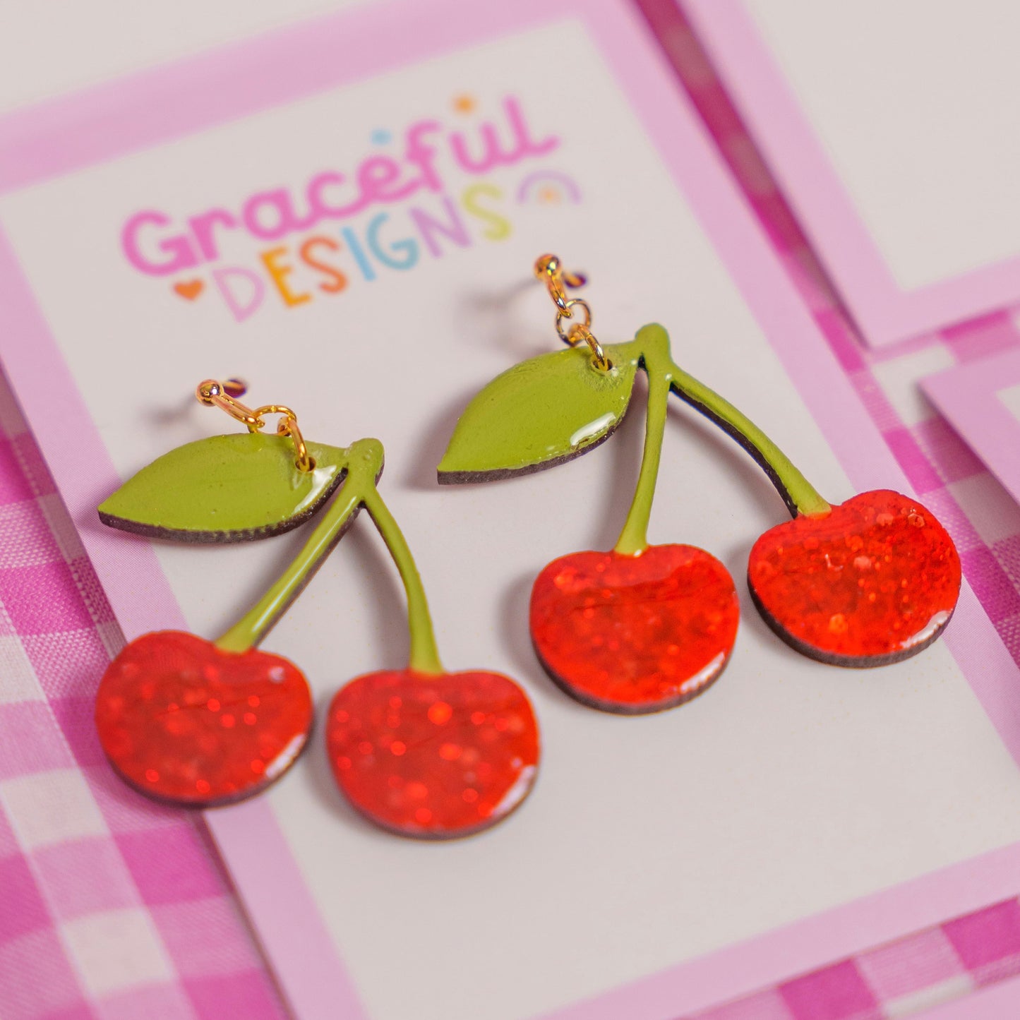 Cherry-themed earrings on a 'Graceful Designs' card with a pink checkered background