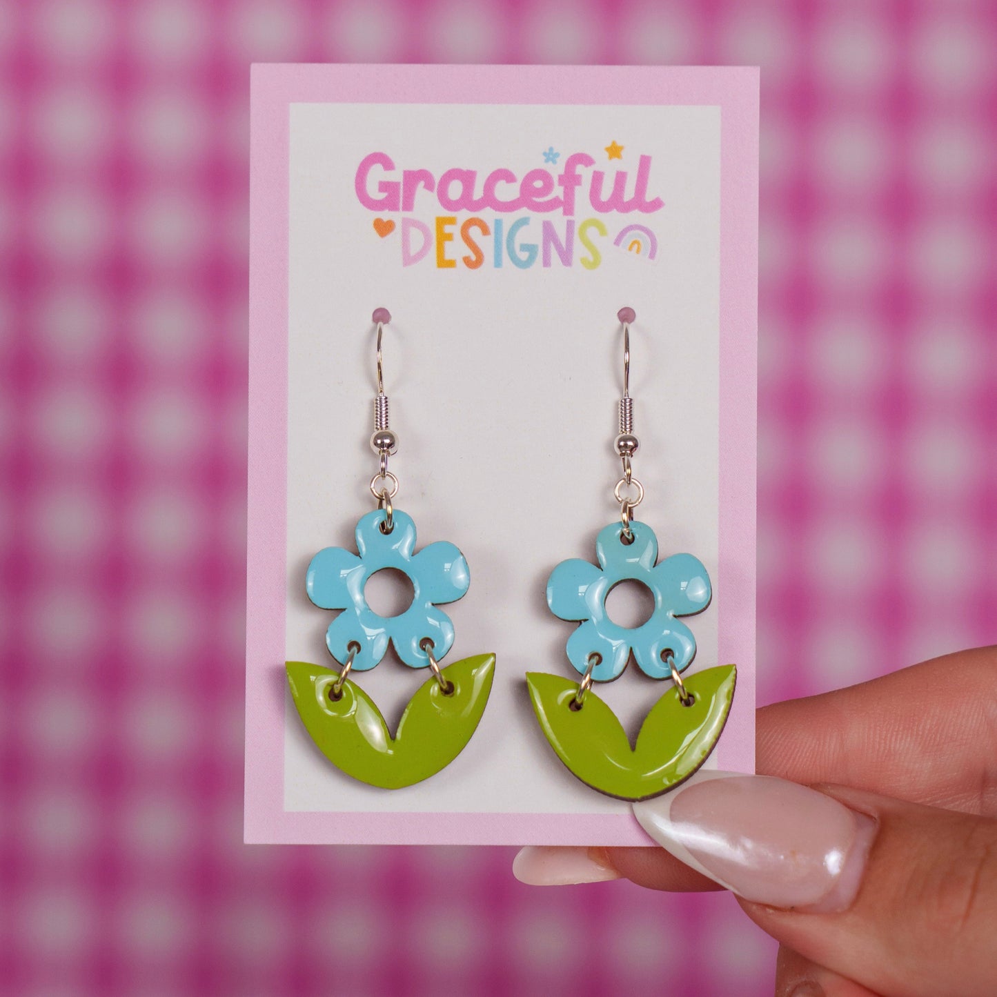 Flower-shaped earrings on a 'Graceful Designs' card against a pink checkered background