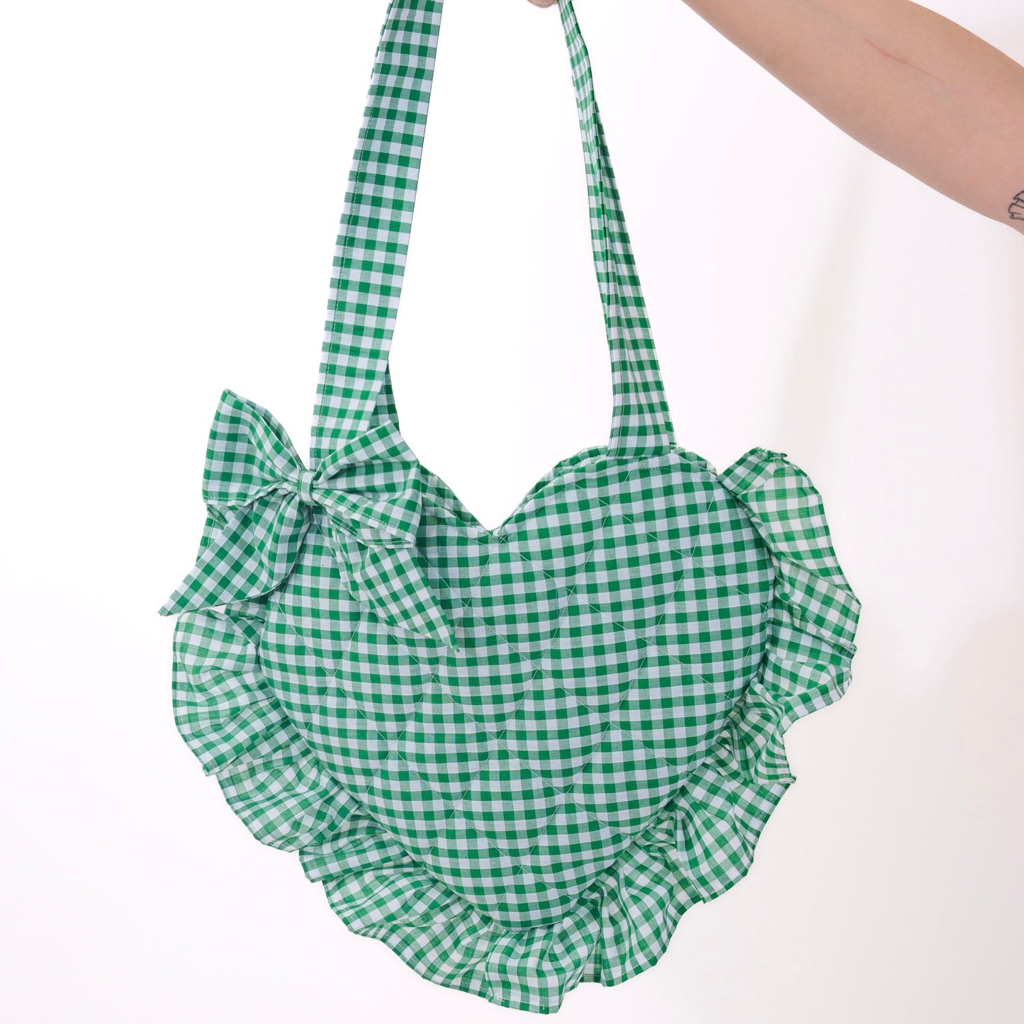 Green checkered bag with ruffles held by a hand on a white background