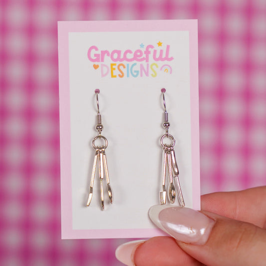 Silver cutlery earrings on a 'Graceful Designs' card against a pink checkered background.