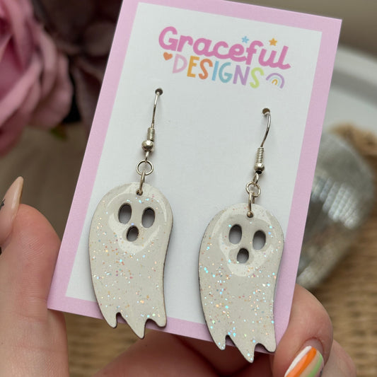 White ghost-shaped earrings on a 'Graceful Designs' card held by a person.