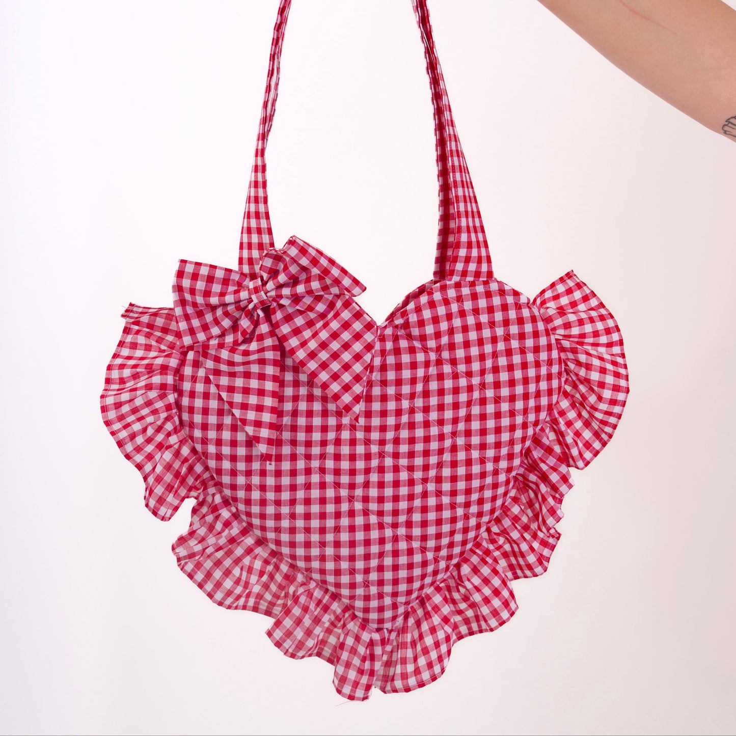 Red and white checkered bag with ruffled details held by a hand on a white background