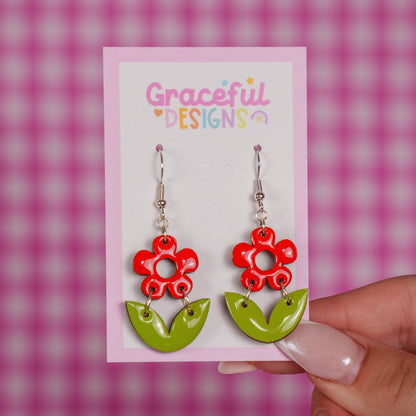 Flower-shaped earrings on a 'Graceful Designs' card against a pink checkered background