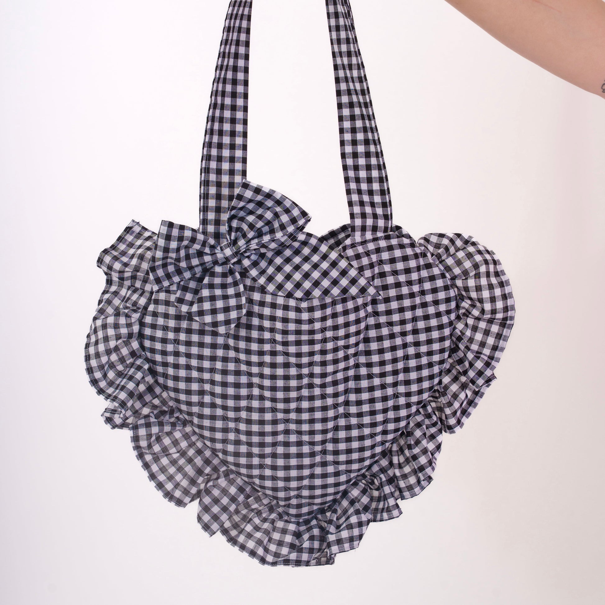 Hand holding a black and white checkered bag with ruffled details on a white background