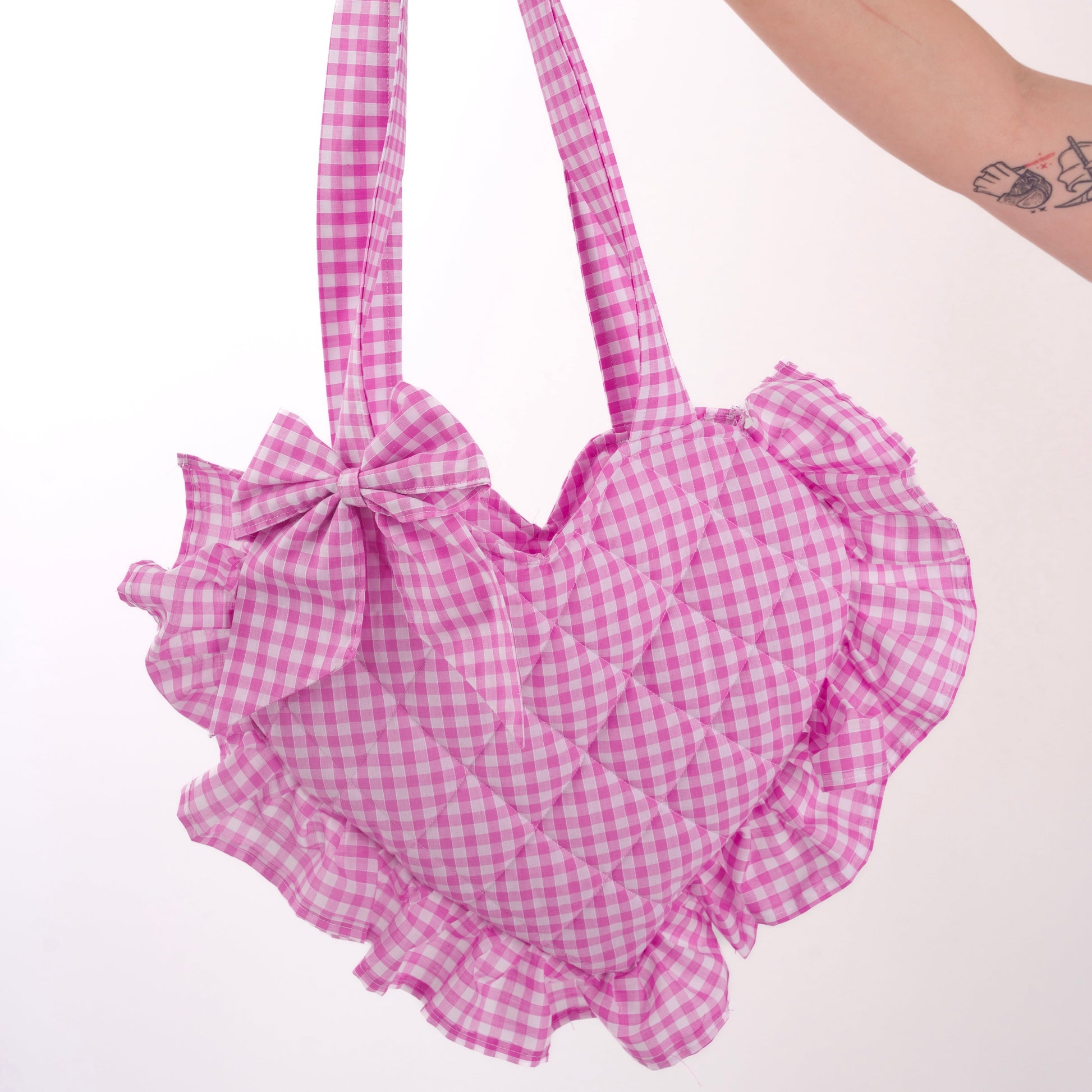 Pink gingham handbag with ruffles held by a hand on a white background