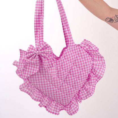 Pink gingham handbag with ruffles held by a hand on a white background