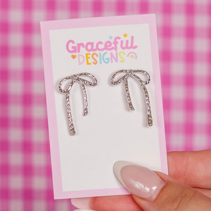 Silver bow-shaped earrings on a 'Graceful Designs' card against a pink checkered background.