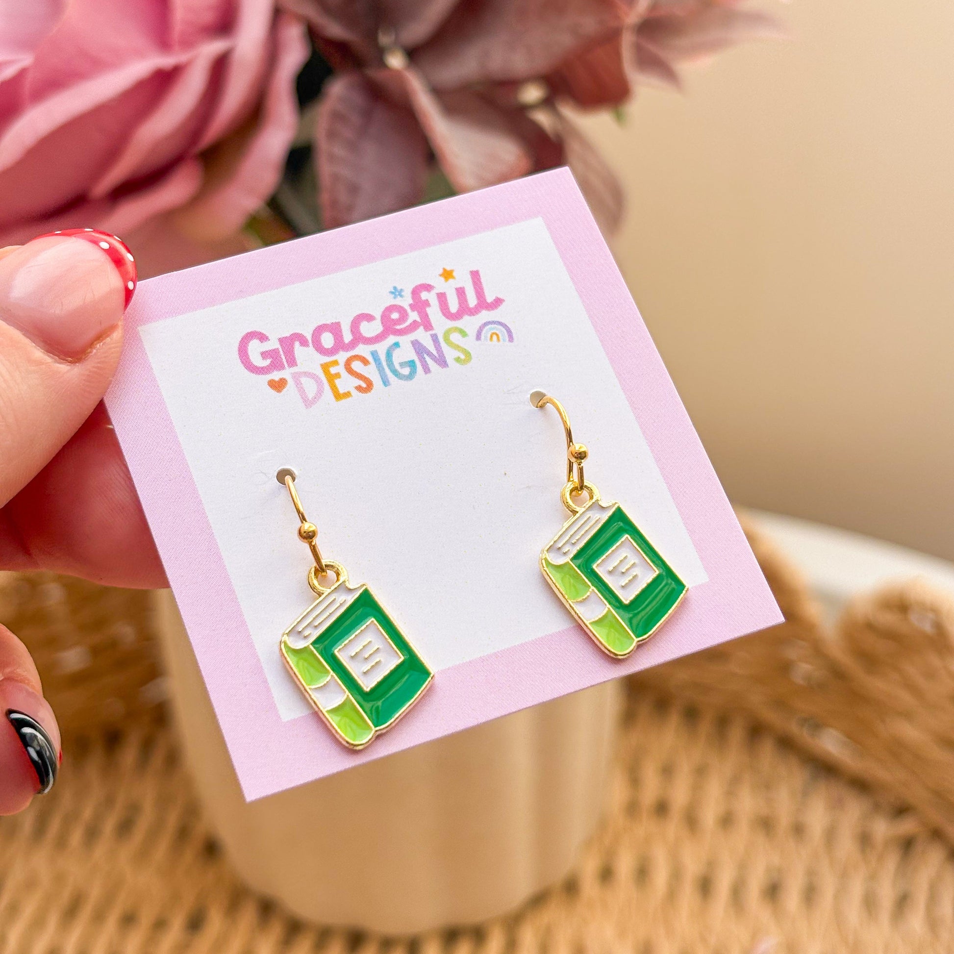 Book-shaped earrings on a 'Graceful Designs' card with flowers in the background