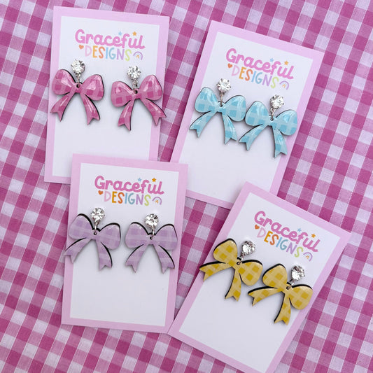 Set of bow-shaped earrings on cards with 'Graceful Designs' branding on a pink checkered background.