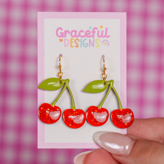 Cherry-themed earrings on a card with 'Graceful Designs' branding against a pink checkered background.