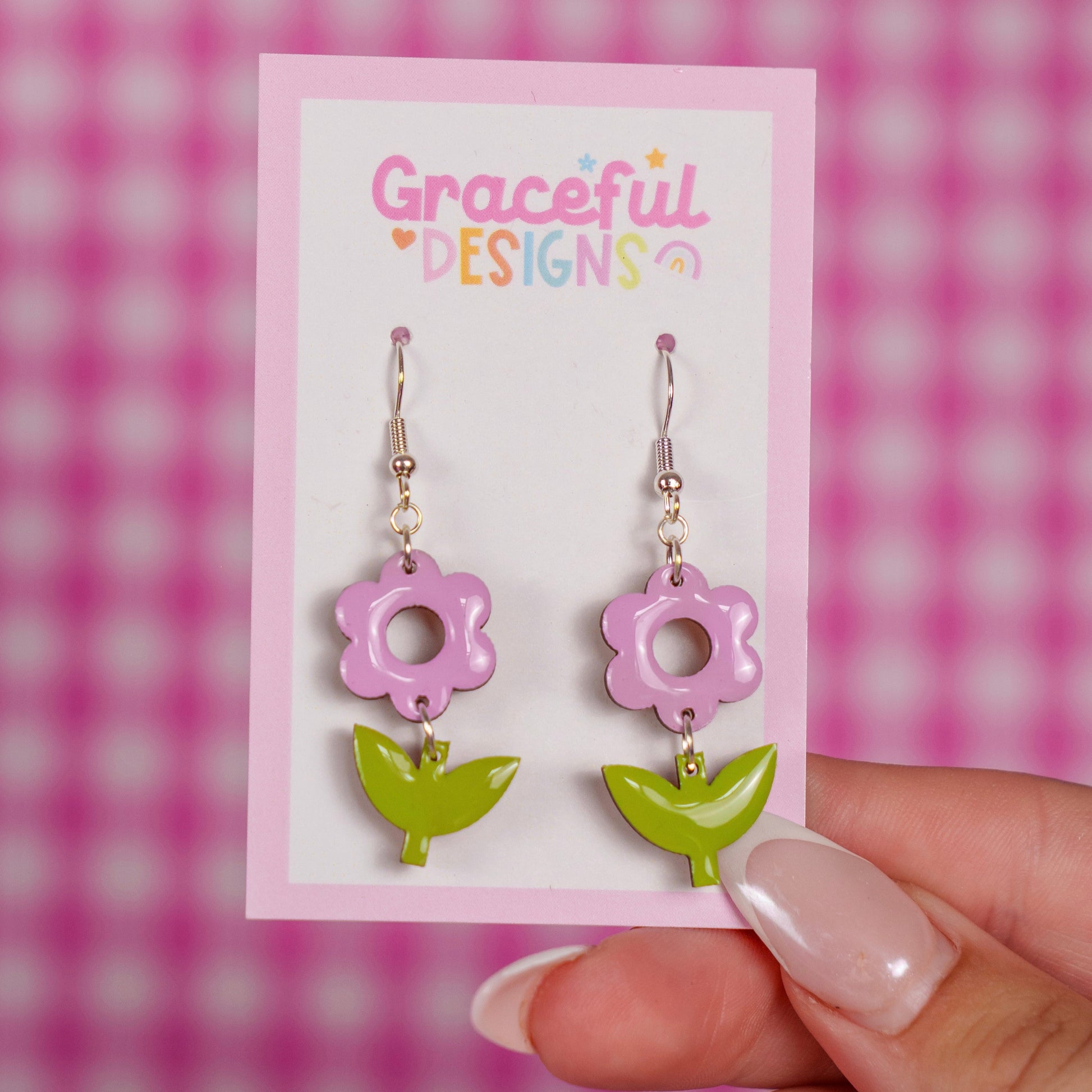 Flower-shaped earrings on a 'Graceful Designs' card against a pink checkered background