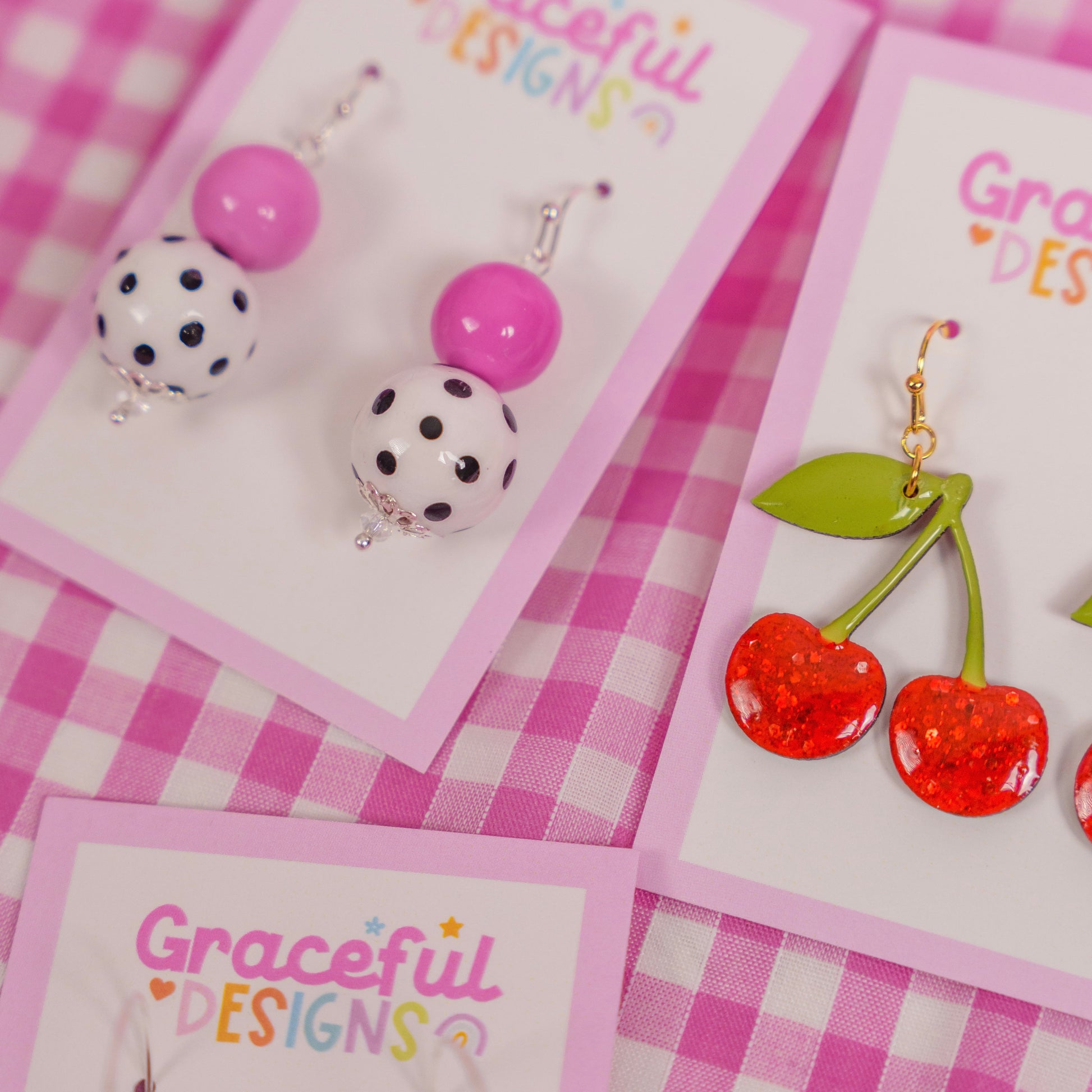 Earrings on cards with 'Graceful Designs' branding on a pink checkered background