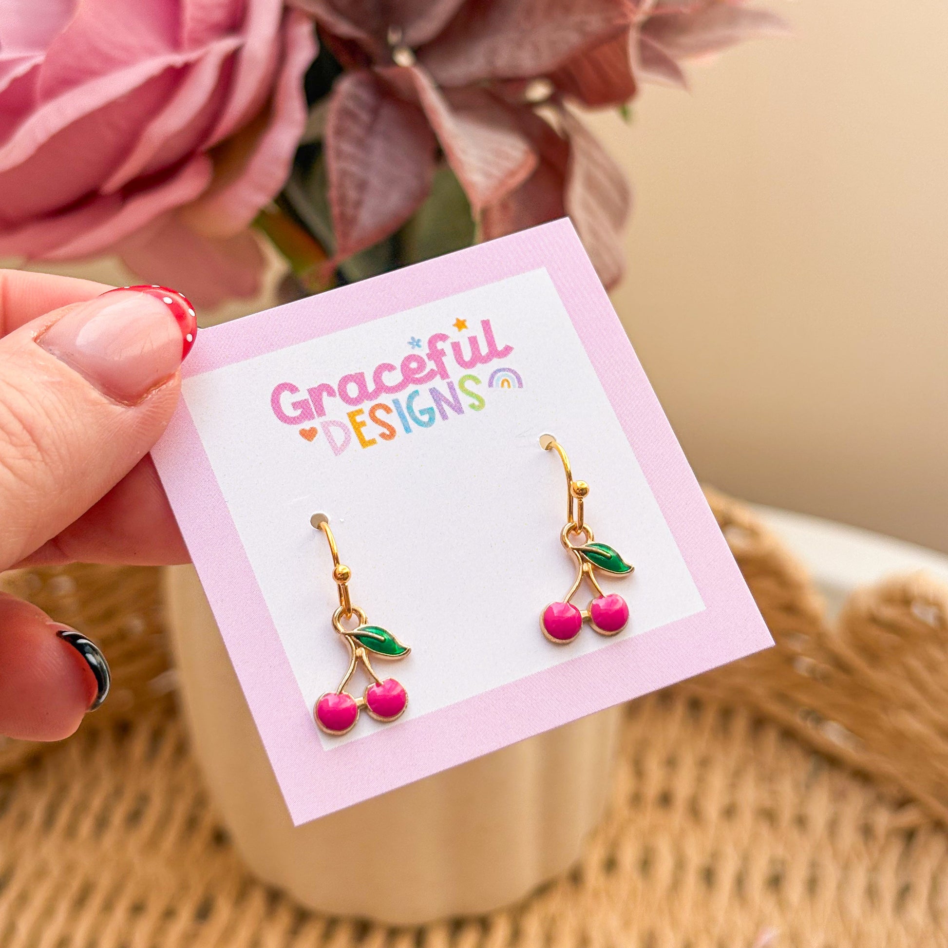 Cherry-themed earrings on a 'Graceful Designs' card with flowers in the background