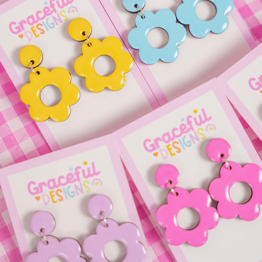 Colorful flower-shaped earrings on 'Graceful Designs' branded cards with a pink checkered background.