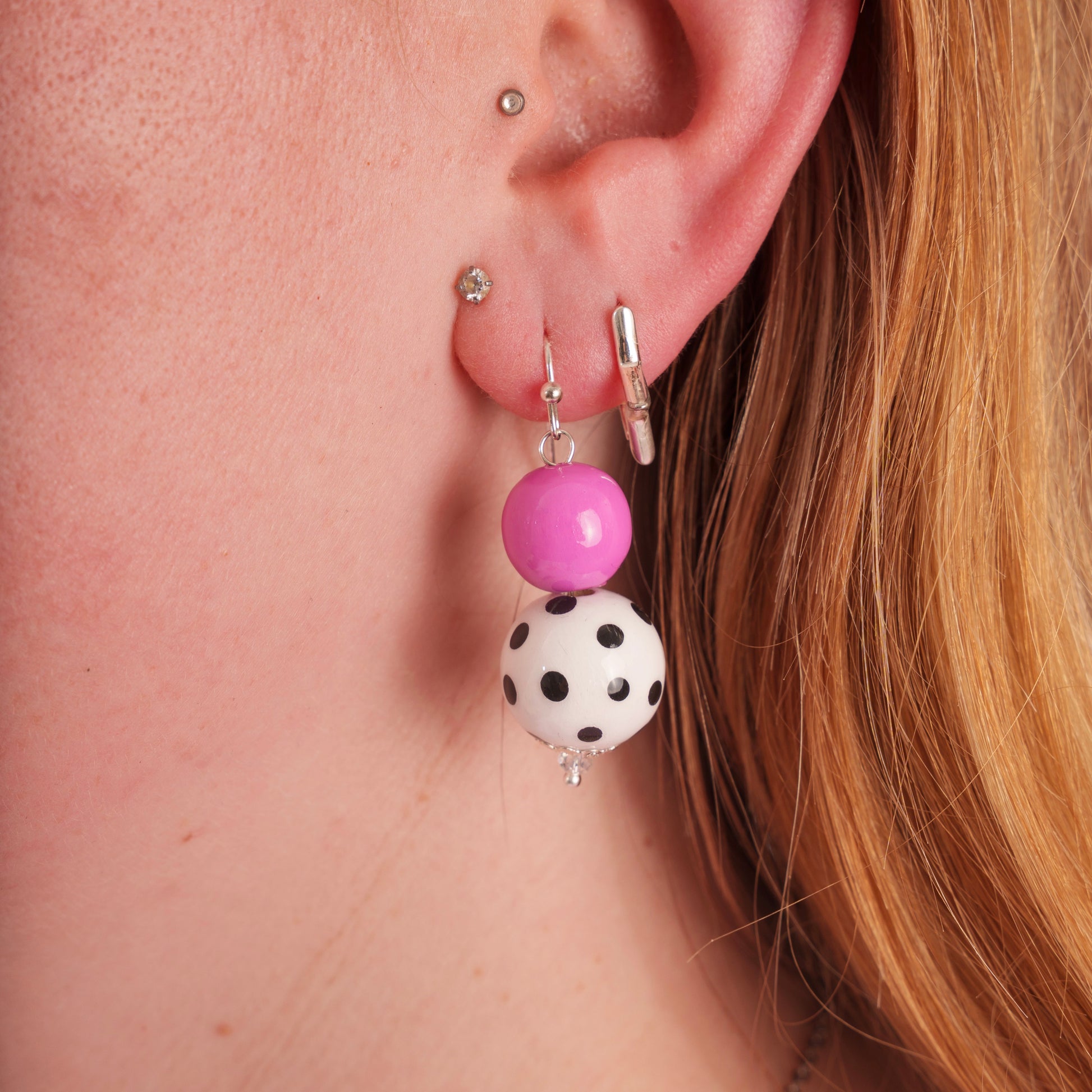 Close-up of an ear wearing a pink and black polka dot earring.