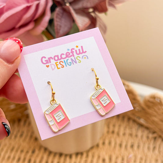 Pink book-shaped earrings on a 'Graceful Designs' card with flowers in the background