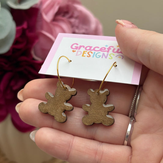 Gold bear-shaped earrings held by a hand with a 'Graceful Designs' tag in the background.