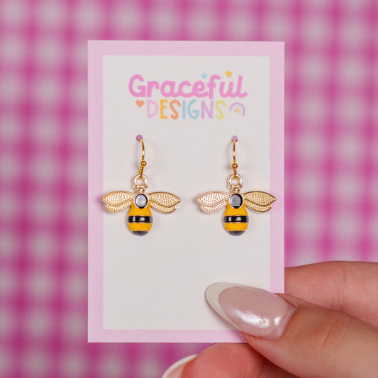 Bee-shaped earrings on a 'Graceful Designs' card against a pink checkered background