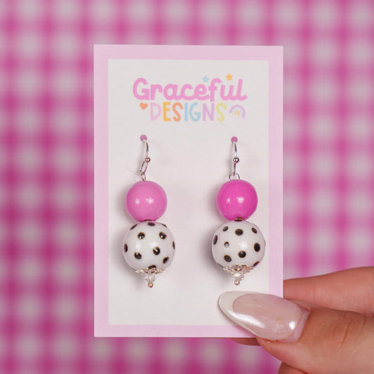 Pair of earrings on a 'Graceful Designs' card against a pink checkered background